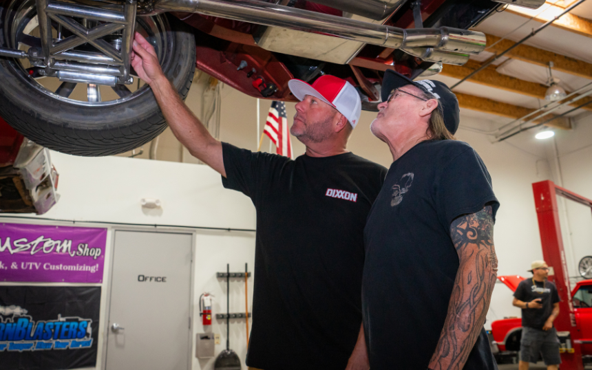 Travis, owner and CEO, discussing with a mechanic while pointing at something under a suspended car.